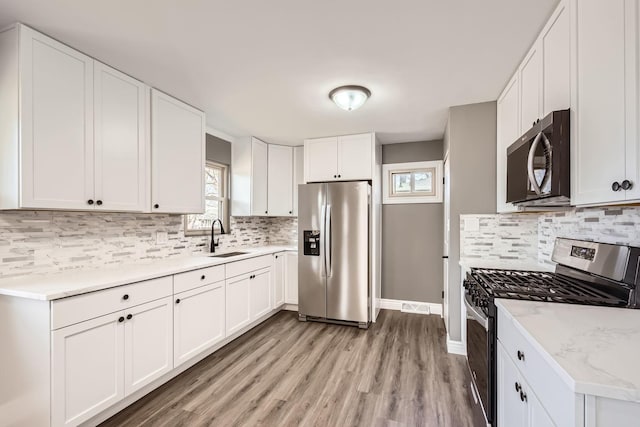 kitchen featuring sink, stainless steel appliances, light hardwood / wood-style flooring, decorative backsplash, and white cabinets