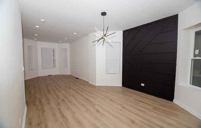 spare room with a notable chandelier and light wood-type flooring