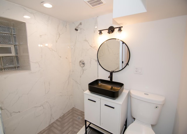 bathroom with a tile shower, vanity, and toilet