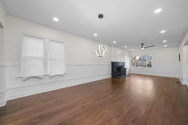 unfurnished living room featuring ceiling fan with notable chandelier and dark hardwood / wood-style flooring