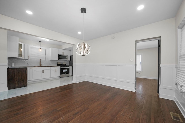 kitchen featuring backsplash, white cabinets, sink, appliances with stainless steel finishes, and decorative light fixtures