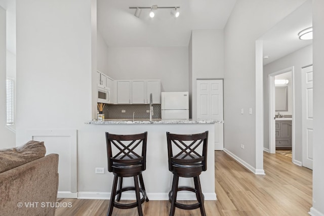 kitchen with kitchen peninsula, tasteful backsplash, white appliances, light hardwood / wood-style flooring, and white cabinetry