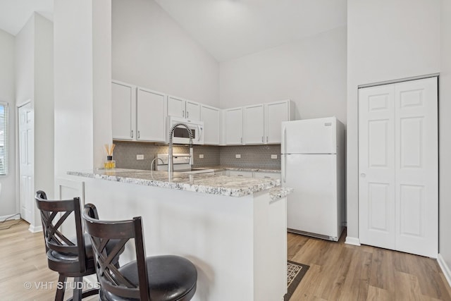 kitchen featuring kitchen peninsula, white cabinetry, high vaulted ceiling, and white appliances