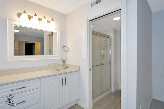 bathroom with vanity, a shower with shower door, and a textured ceiling