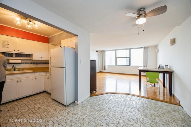 kitchen with a sink, freestanding refrigerator, white cabinetry, a ceiling fan, and baseboards