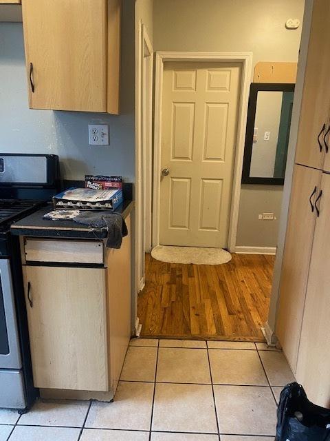 kitchen with white gas stove, light tile patterned floors, and light brown cabinetry