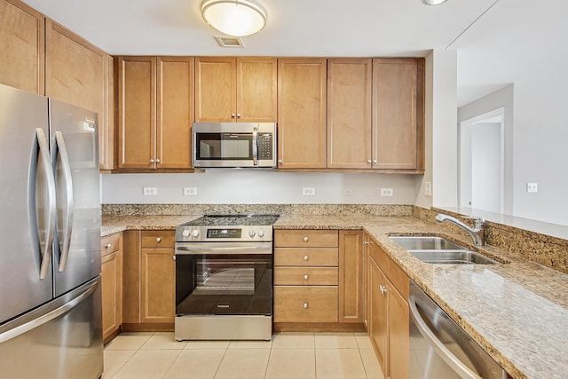 kitchen with stainless steel appliances, light tile patterned flooring, light stone countertops, and sink