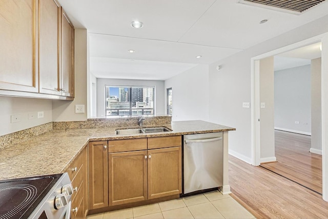 kitchen with sink, light tile patterned floors, appliances with stainless steel finishes, light stone counters, and kitchen peninsula