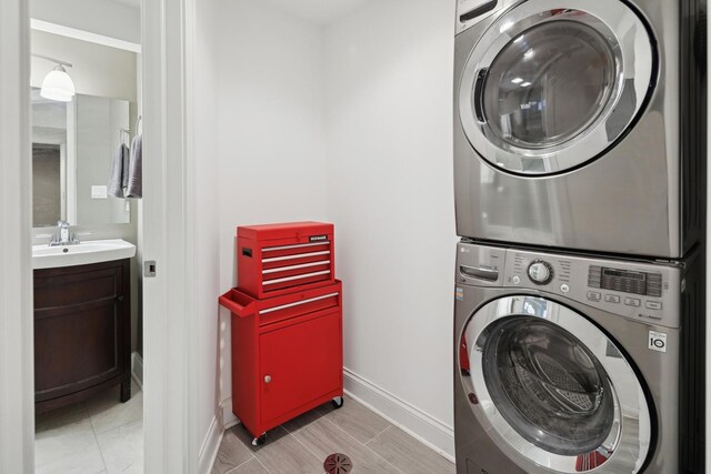 laundry area with baseboards, laundry area, stacked washing maching and dryer, light tile patterned flooring, and a sink