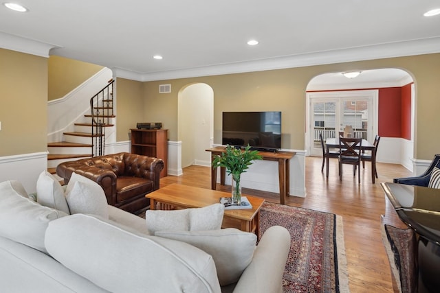 living room featuring visible vents, arched walkways, light wood-style flooring, and stairway