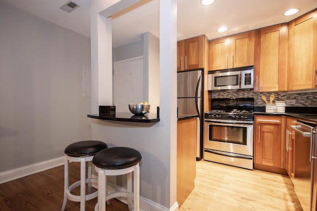 kitchen featuring decorative backsplash, a kitchen bar, light wood-type flooring, and stainless steel appliances