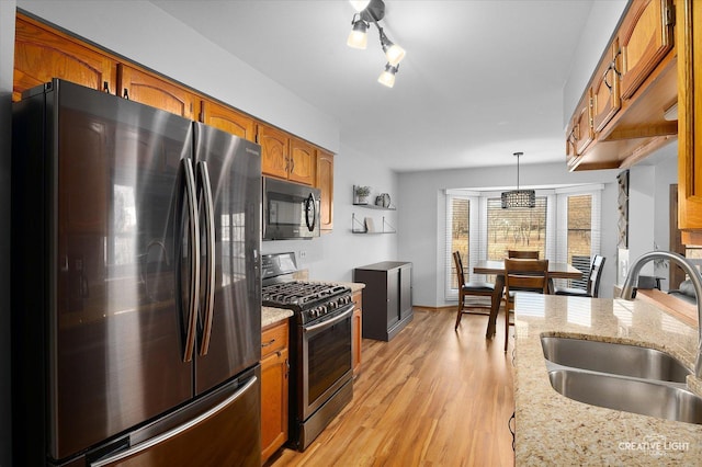 kitchen with sink, hanging light fixtures, light stone counters, light hardwood / wood-style flooring, and appliances with stainless steel finishes