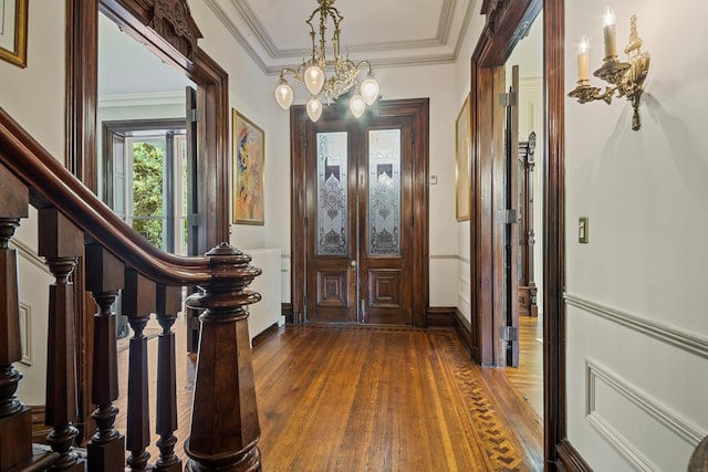 foyer entrance featuring dark hardwood / wood-style flooring, ornamental molding, french doors, and an inviting chandelier