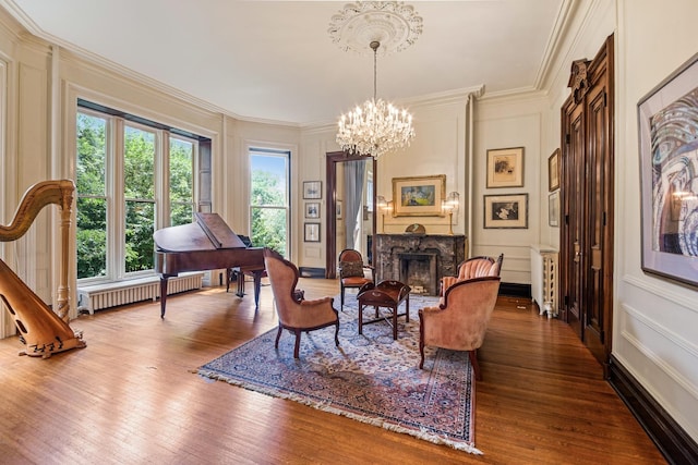 sitting room with wood-type flooring, a high end fireplace, radiator, ornamental molding, and an inviting chandelier