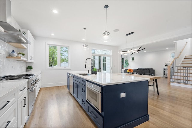 kitchen featuring light wood-style flooring, a sink, white cabinetry, blue cabinetry, and wall chimney range hood