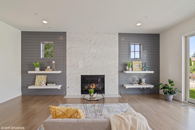 living room with a wealth of natural light, recessed lighting, wood finished floors, and a high end fireplace