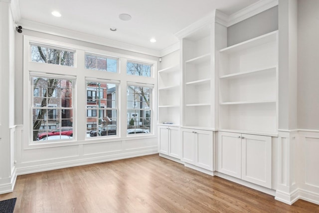 empty room with light hardwood / wood-style flooring, built in features, and ornamental molding