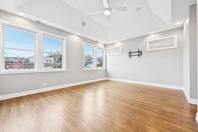 empty room with a tray ceiling, ceiling fan, hardwood / wood-style floors, and vaulted ceiling