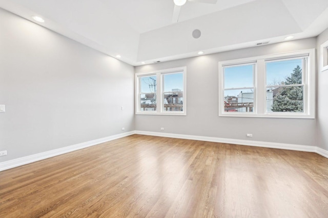 empty room with ceiling fan, light wood-type flooring, and a tray ceiling