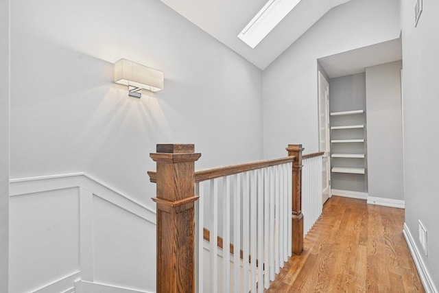 hall with lofted ceiling with skylight and light hardwood / wood-style flooring