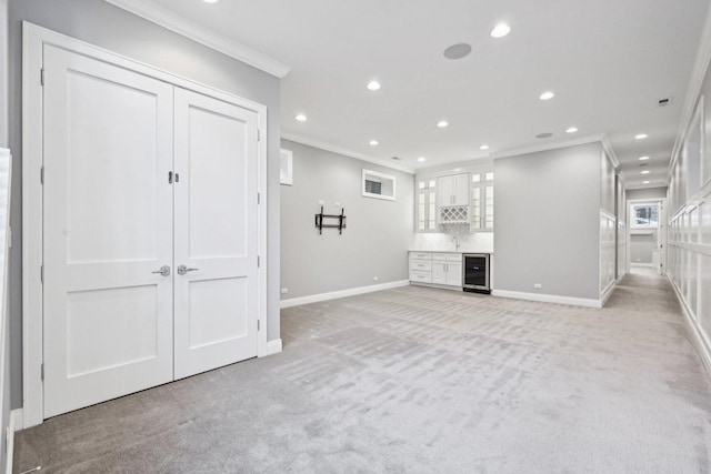 unfurnished living room featuring plenty of natural light, ornamental molding, light carpet, and wine cooler