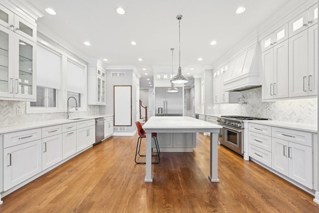 kitchen with hardwood / wood-style flooring, custom exhaust hood, white cabinetry, and appliances with stainless steel finishes