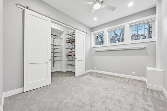 unfurnished bedroom with a barn door, ceiling fan, and light colored carpet