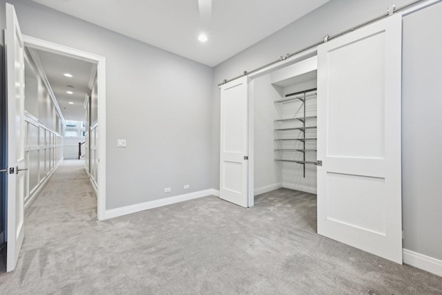 unfurnished bedroom featuring ceiling fan, a barn door, light colored carpet, and a closet