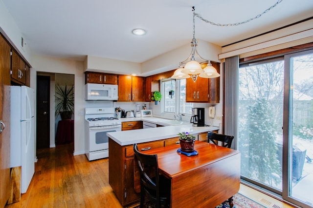 kitchen featuring white appliances, a healthy amount of sunlight, hanging light fixtures, and light wood-type flooring