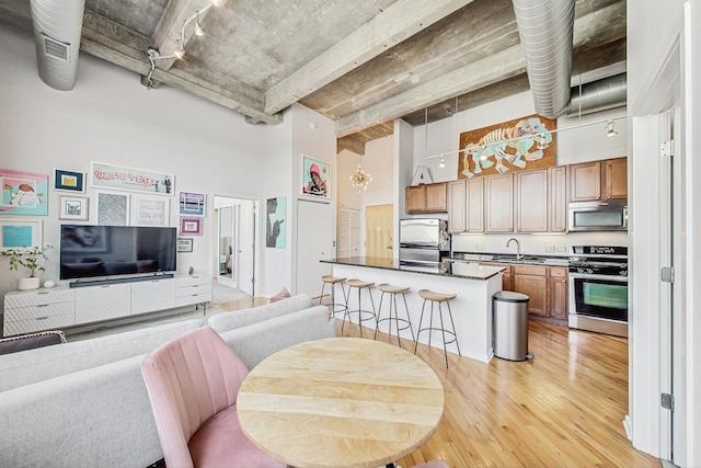 kitchen with a high ceiling, sink, a breakfast bar area, light wood-type flooring, and stainless steel appliances