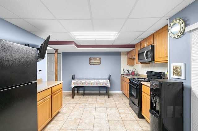 kitchen with a drop ceiling, light tile patterned floors, black appliances, and sink