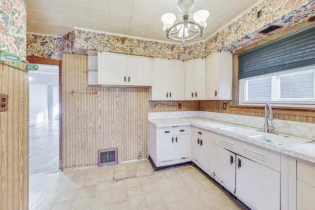 kitchen with wood walls, white cabinetry, a notable chandelier, and sink