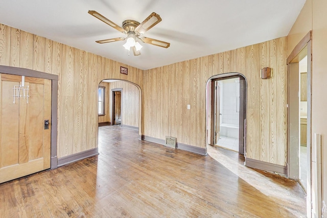 empty room featuring hardwood / wood-style floors, ceiling fan, and wood walls