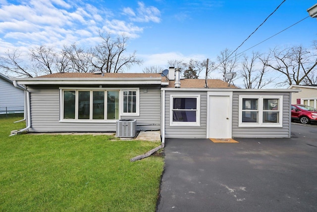 rear view of property with central AC unit and a lawn