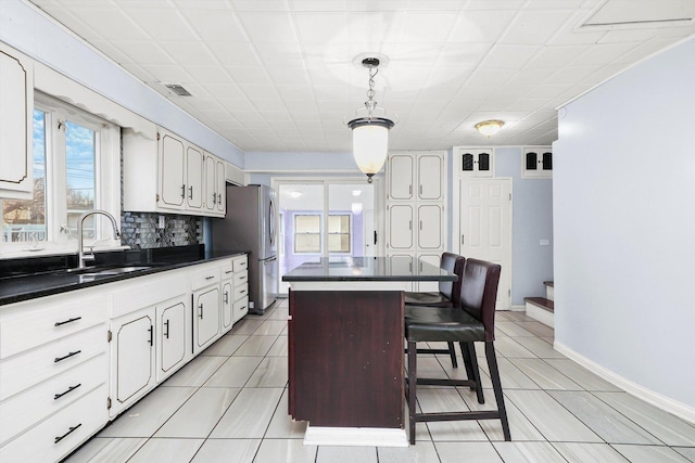 kitchen featuring stainless steel refrigerator, white cabinetry, a center island, decorative light fixtures, and decorative backsplash