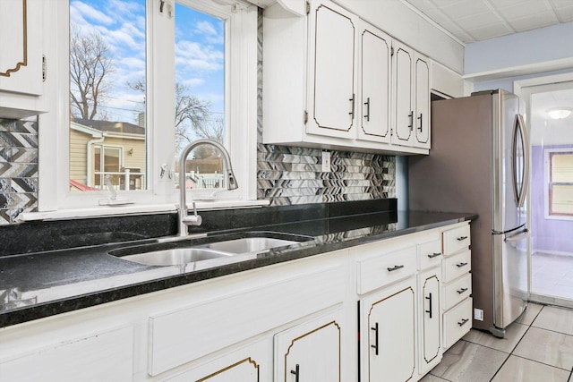 kitchen featuring stainless steel fridge, backsplash, sink, light tile patterned floors, and white cabinetry