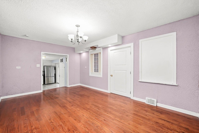 empty room with wood-type flooring, a textured ceiling, and a chandelier