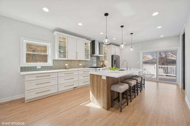 kitchen featuring tasteful backsplash, an island with sink, stainless steel appliances, wall chimney range hood, and a sink