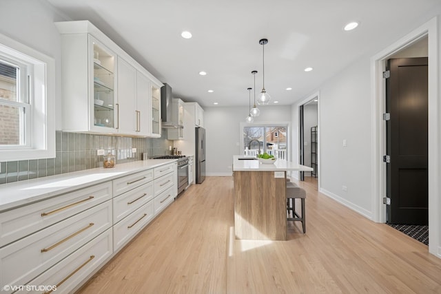 kitchen featuring appliances with stainless steel finishes, a sink, light wood-type flooring, wall chimney range hood, and backsplash