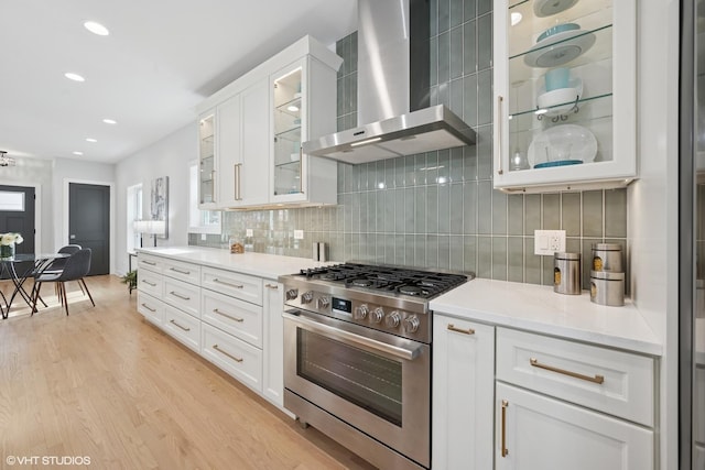 kitchen with white cabinets, decorative backsplash, light wood-style flooring, wall chimney range hood, and stainless steel range with gas stovetop