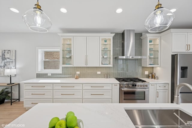 kitchen featuring decorative backsplash, wall chimney exhaust hood, decorative light fixtures, stainless steel appliances, and a sink