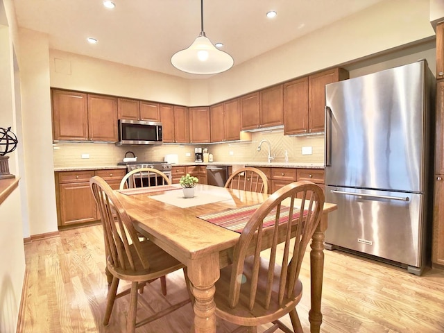 kitchen featuring light wood-type flooring, tasteful backsplash, stainless steel appliances, sink, and pendant lighting