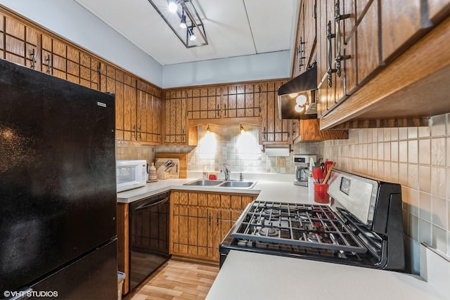 kitchen with brown cabinetry, under cabinet range hood, light countertops, black appliances, and a sink