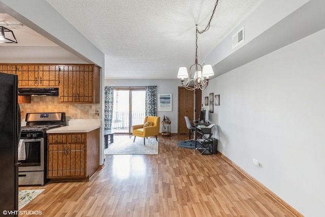 kitchen with brown cabinets, light countertops, visible vents, freestanding refrigerator, and stainless steel range with gas stovetop