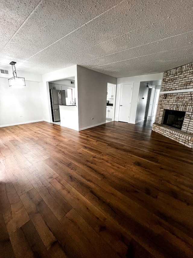 unfurnished living room with a fireplace, a textured ceiling, and dark hardwood / wood-style floors