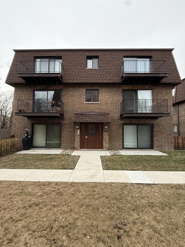 view of front facade with a balcony, a patio, and a front lawn