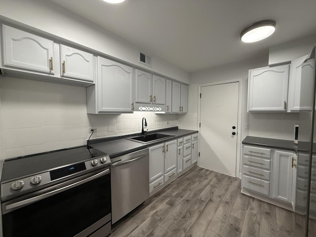 kitchen with hardwood / wood-style floors, white cabinets, sink, decorative backsplash, and appliances with stainless steel finishes