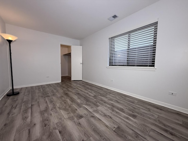 unfurnished bedroom with dark hardwood / wood-style floors and a walk in closet