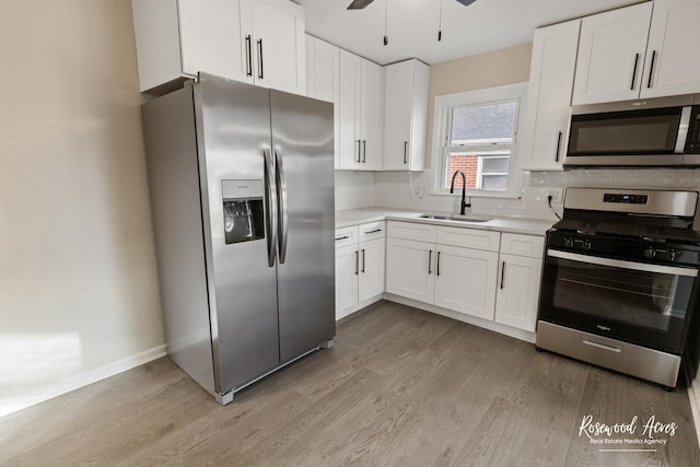 kitchen with appliances with stainless steel finishes, light wood-type flooring, ceiling fan, sink, and white cabinets