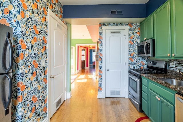 kitchen featuring light wood-type flooring, dark stone counters, stainless steel appliances, sink, and green cabinetry